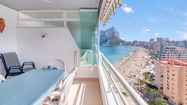 Een balkon met een bed, stoelen en uitzicht op een strand en stadsgezicht.
