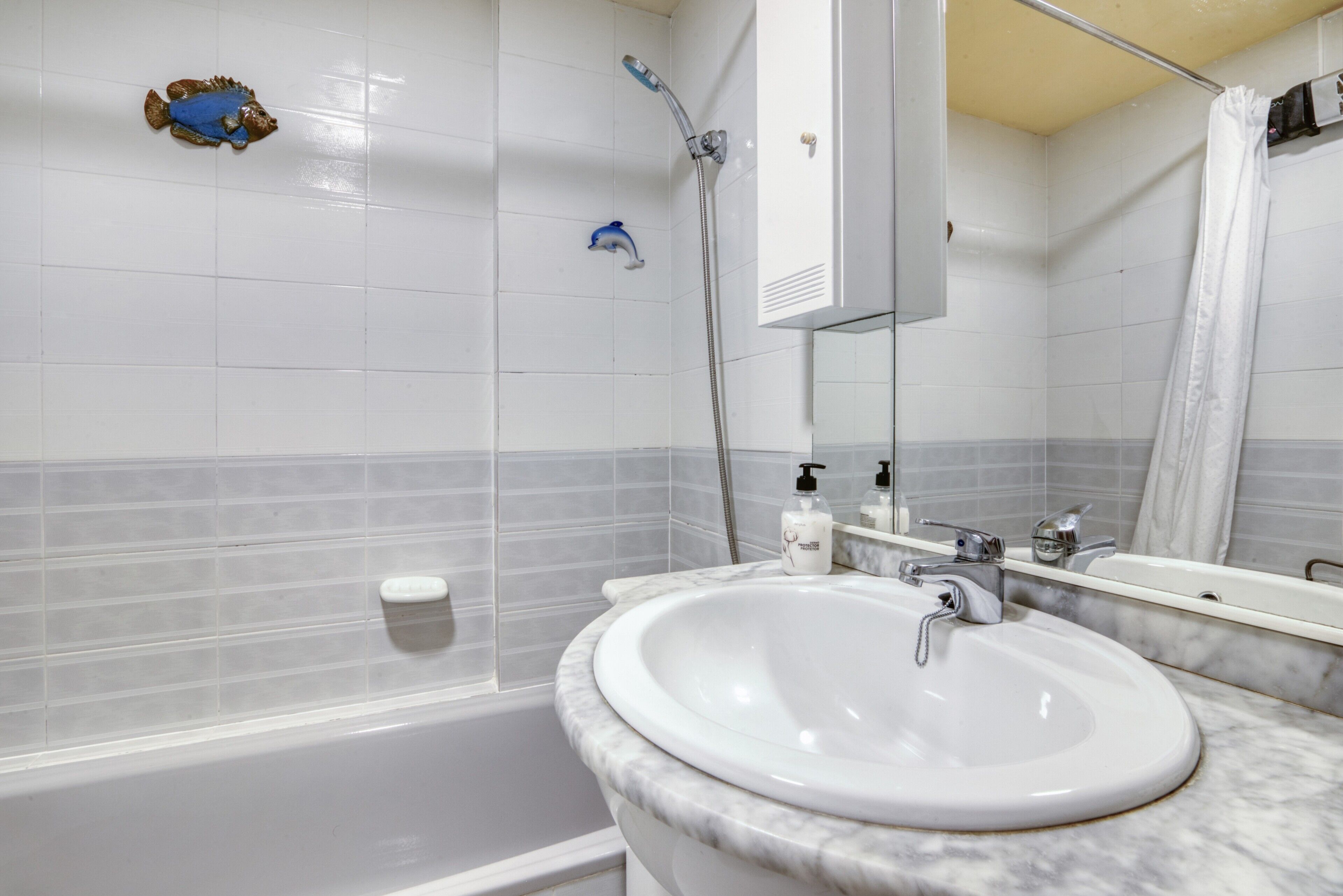 Un baño con bañera, lavamanos blanco, espejo y cabezal de ducha.