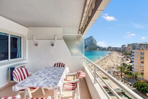 Un balcón con mesa y sillas, con vista a una playa y una montaña.