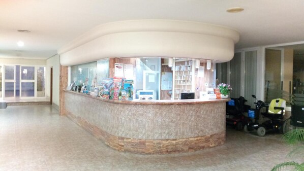 A reception desk with a curved design, a glass partition, and a counter with various items.