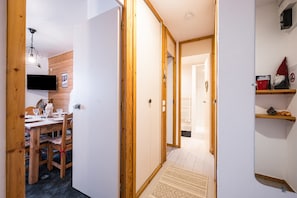 Un couloir avec des portes en bois, un coin repas avec une table et des chaises, et une étagère décorée d’une figurine de gnome.