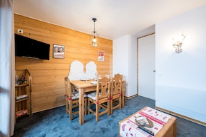 Una habitación con paneles de madera, una mesa de comedor, sillas, un televisor montado en la pared y un candelabro.