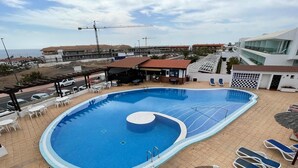 Une piscine sur le toit, dotée de chaises longues, d’un espace bar et offrant une vue sur les bâtiments environnants.