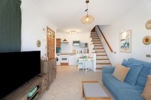 Una sala de estar con televisión, sofá y una escalera que lleva a una cocina.