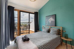 A bedroom with a bed, a view of the outside, a small table, and a wall with a zebra painting.