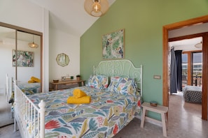 A bedroom with a bed, a bedside table, a mirror, and a view of the outside.