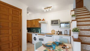 Une cuisine avec des meubles en bois, une table à manger avec des chaises, un lave-linge et un escalier.