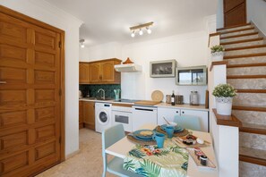 Una cocina con armarios de madera, una mesa de comedor con sillas, una lavadora y una escalera.