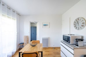 A compact kitchen with a dining table, chairs, a microwave, and a clock on the wall. - Magnificent T2 Next to the Beach – Private Balcony, 2 People, 300 m from the Beach (Seignosse)