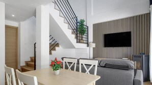 A modern living room with a staircase, a flat-screen TV, a grey sofa, and a dining table with chairs. - Apartment 'En Los Caños De Meca' with Sea View, Wi-Fi and Air Conditioning (Los Caños de Meca)