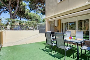 En udendørs terrasse med et bord, stole, en varmtvandsbeholder og udsigt til træer samt en bygning.