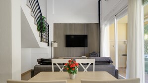 A modern living room with a TV, a dining table with chairs, a sofa, and a staircase. - Apartment 'En Los Caños De Meca' with Sea View, Wi-Fi and Air Conditioning (Los Caños de Meca)