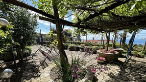 A stone-paved garden with a pergola, potted plants, and a view of the sea.
