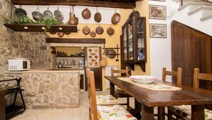 A rustic kitchen with stone walls, wooden beams, and a dining area with a wooden table and chairs.