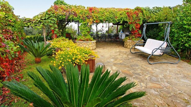 A garden patio with a swing chair, a stone floor, and various plants.