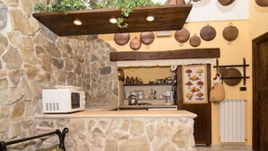 A kitchen with a stone wall, a microwave, a shelf with kitchen items, and a hanging pot rack.