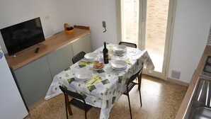Un comedor con una mesa lista para cuatro personas, un televisor y una botella de vino.
