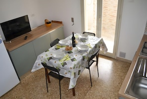 A dining area with a table set for four, a television, and a bottle of wine. - Holiday Home 'Casa A T Dell Orso X 6 Guests' with Private Garden (Torre dell'Orso)