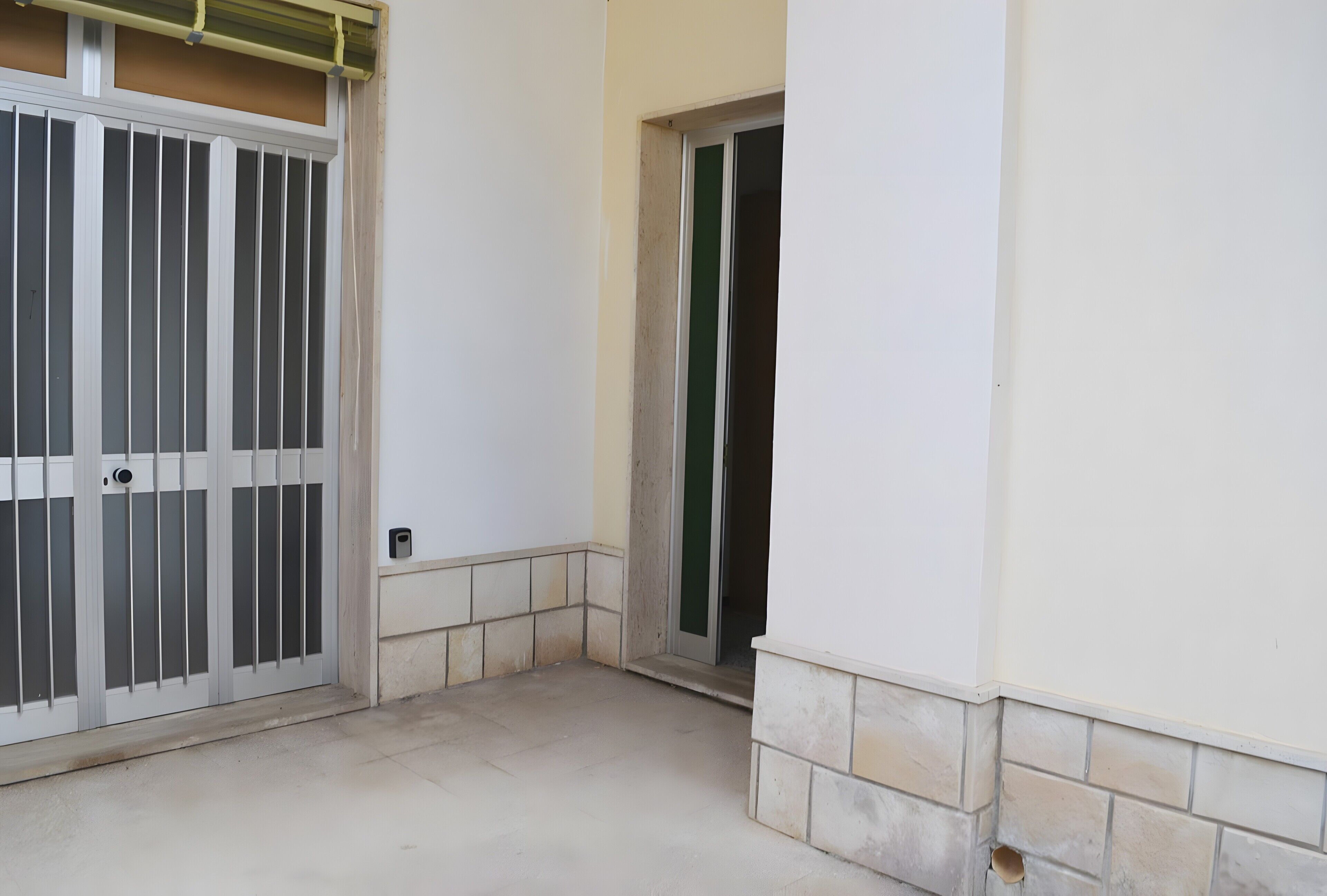 Un couloir avec une porte blanche, une porte verte et un sol carrelé.