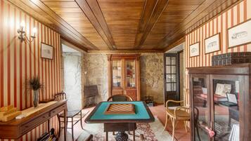 Una habitación con techo de madera, paredes a rayas, una mesa de ajedrez, un aparador con puertas de cristal y una chimenea.