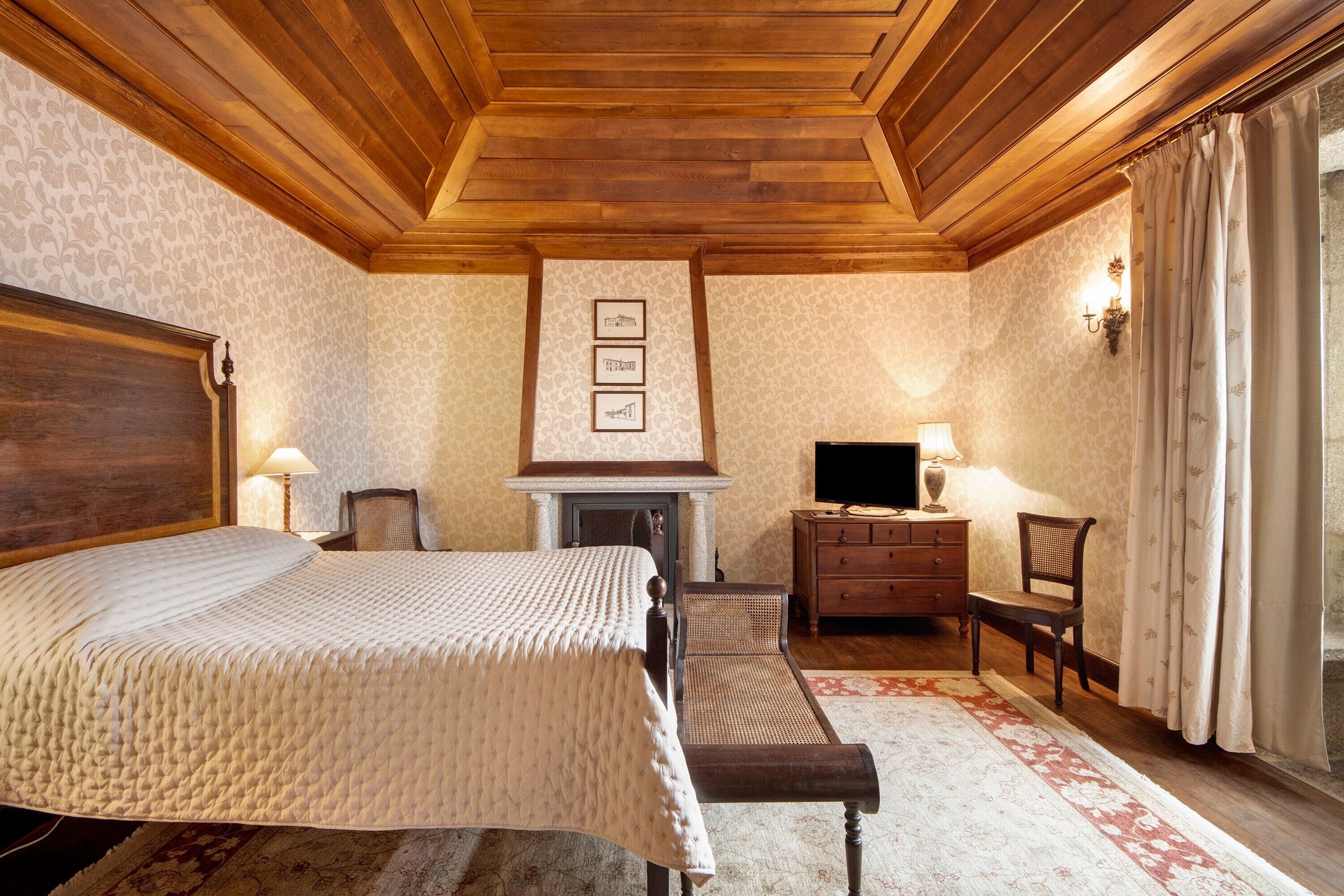 Ein Schlafzimmer mit einem großen Bett, Holzboden, Kamin, Fernseher und Schreibtisch mit Stuhl.