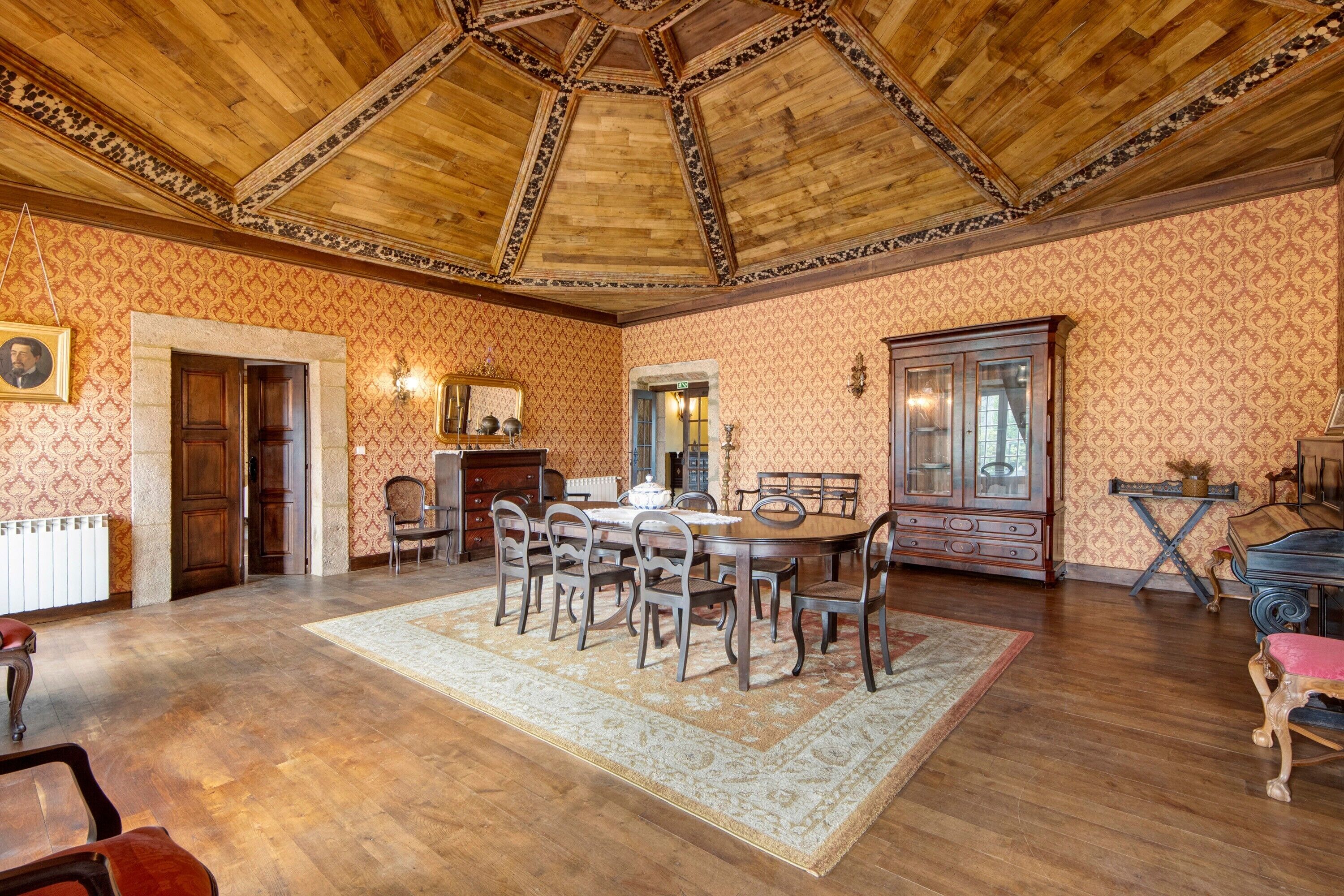 A dining area with a wooden table, chairs, a patterned wallpaper, and a wooden ceiling.