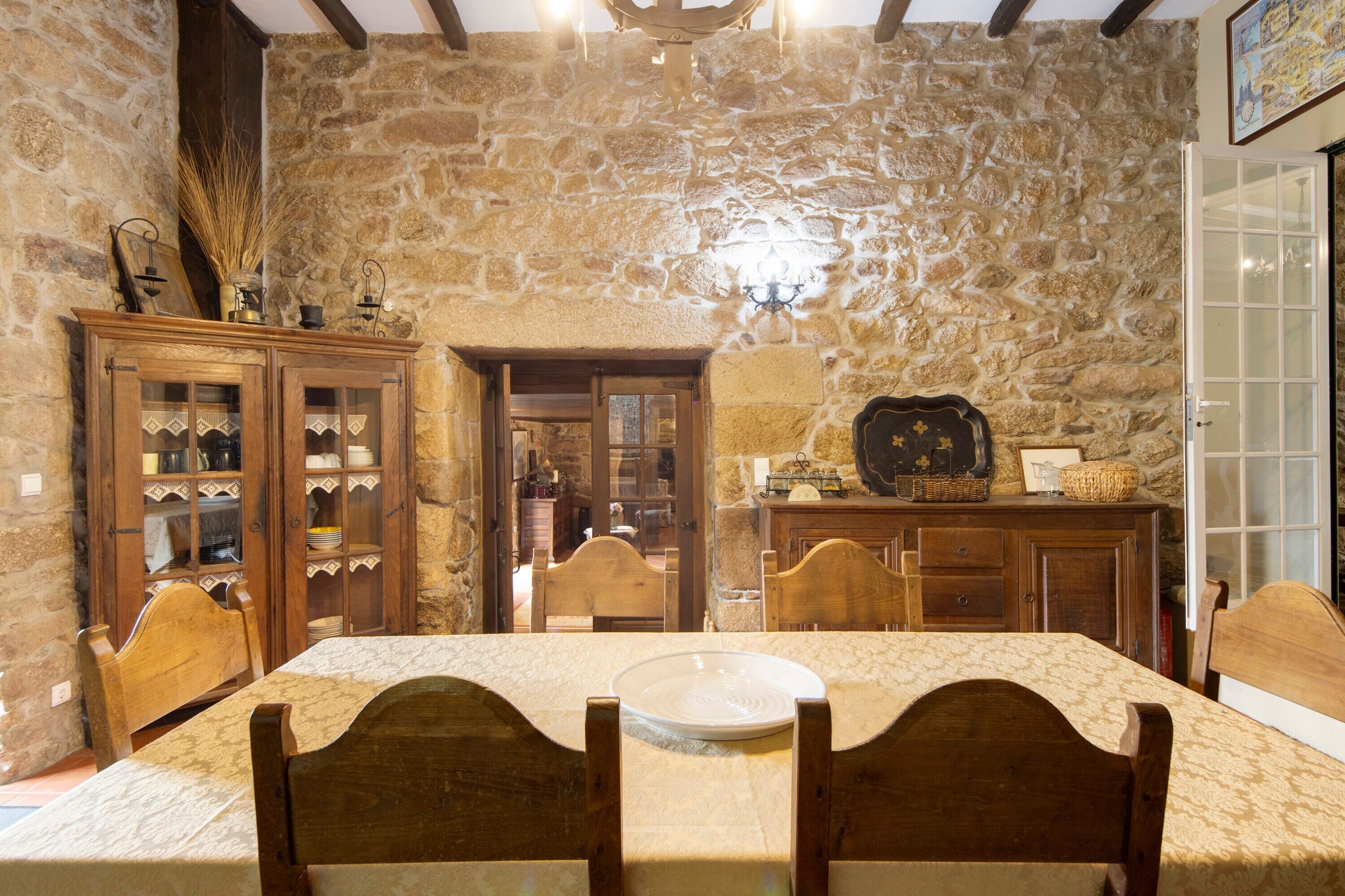 A stone-walled dining area with wooden furniture, a chandelier, and a view into another room.