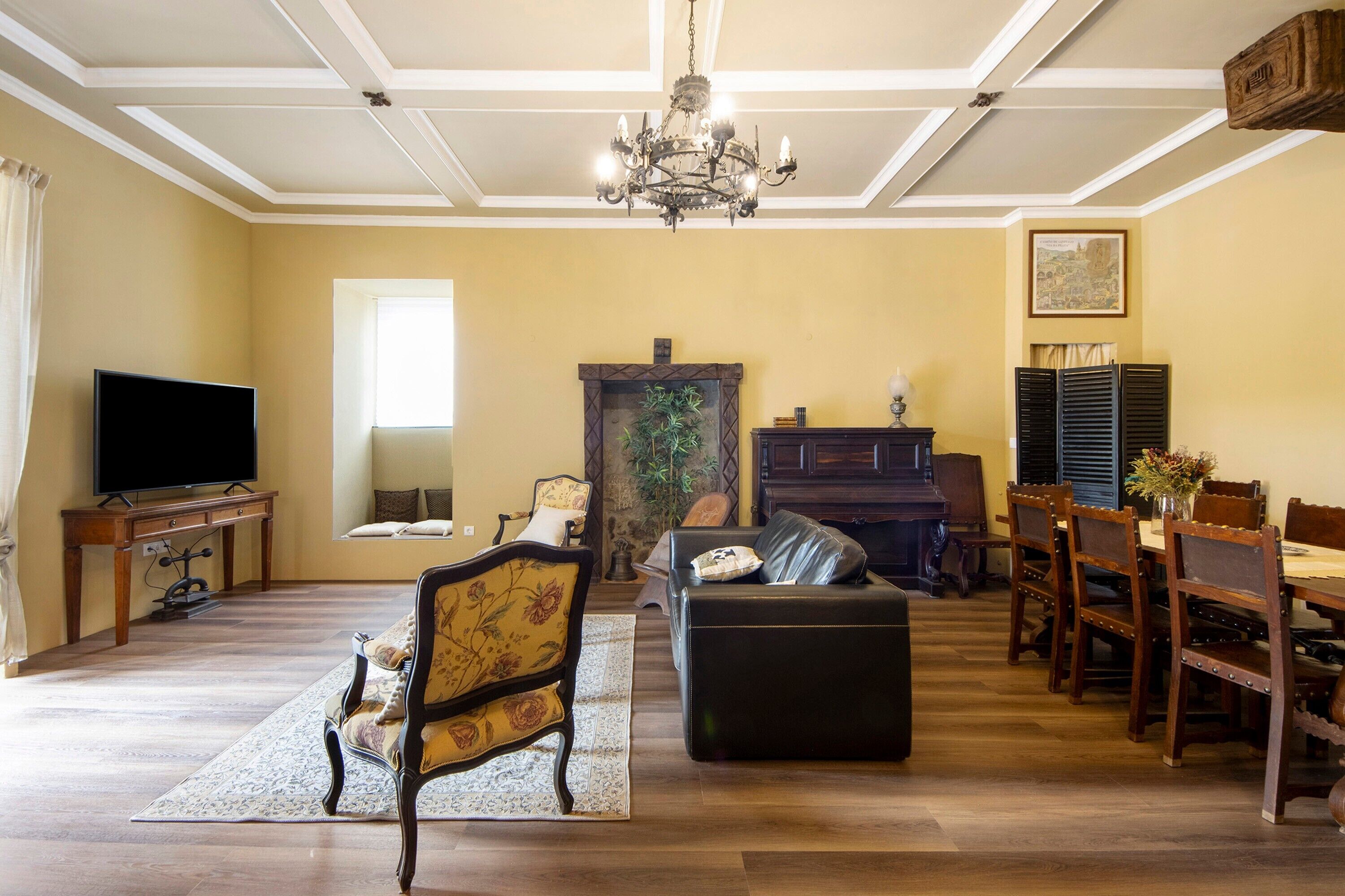 A living room with a television, a fireplace, a piano, a dining table with chairs, and a chandelier.