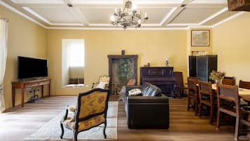 A living room with a television, a fireplace, a piano, a dining table with chairs, and a chandelier.