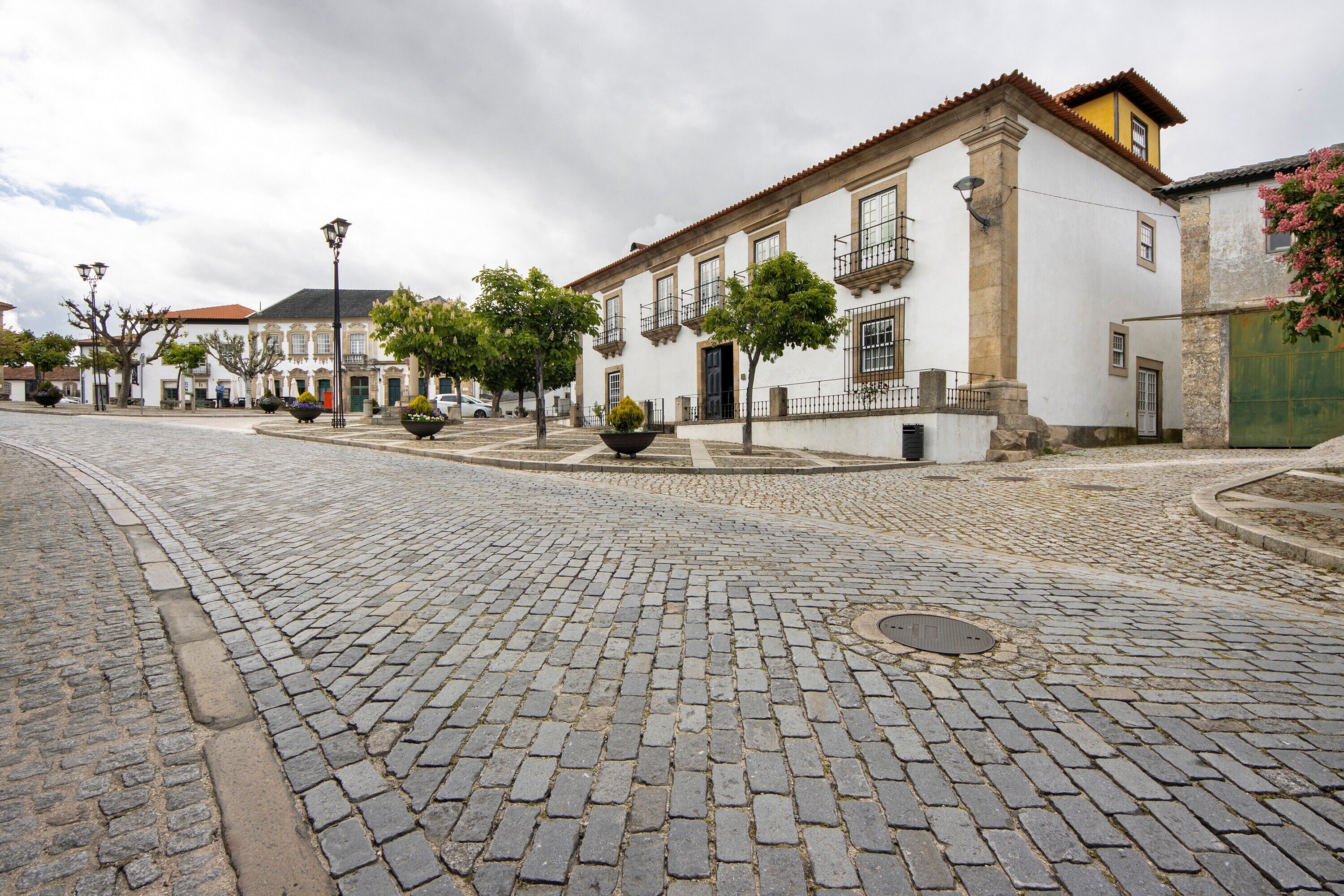 A cobblestone street with historic buildings, a central roundabout, and a fountain.
