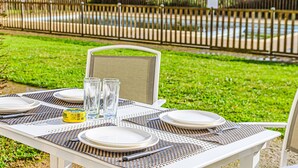 An outdoor dining table set with plates, glasses, and cutlery, surrounded by a lush green lawn and a wooden fence. - Le Château de Kergonano by Interhome (Baden)