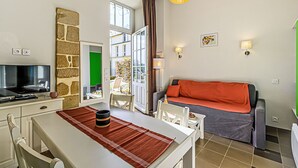 A modern living room with a sofa, a dining table with chairs, a television, and a large window. - Le Château de Kergonano by Interhome (Baden)
