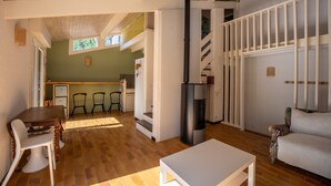 A spacious living area with a wooden floor, a white sofa, a dining table with chairs, a kitchen in the background, and a staircase with a railing. - Holiday home Le Penon – Terrace, balcony, Wi-Fi, 6 guests, close to Seignosse beach (Seignosse)