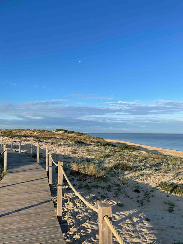 A wooden boardwalk leading to a beach with dunes and a clear sky.