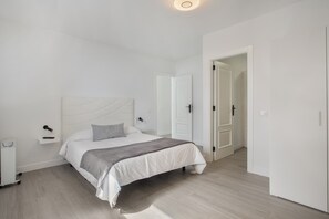 Un dormitorio con cama, mesitas de noche y una puerta que da a otra habitación.