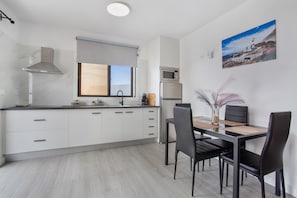 A modern kitchen with white cabinets, a stainless steel range hood, a microwave, and a dining area with a table and chairs.