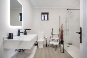 A modern bathroom with a large mirror, a white sink, a toilet, and a glass shower enclosure.