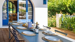 A dining table set for six with plates, cutlery, and wine glasses, overlooking a garden. - Iparra Holiday Home – Hossegor Golf – 12 Guests, Private Pool, A/C, Near the Beach (Soorts-Hossegor)