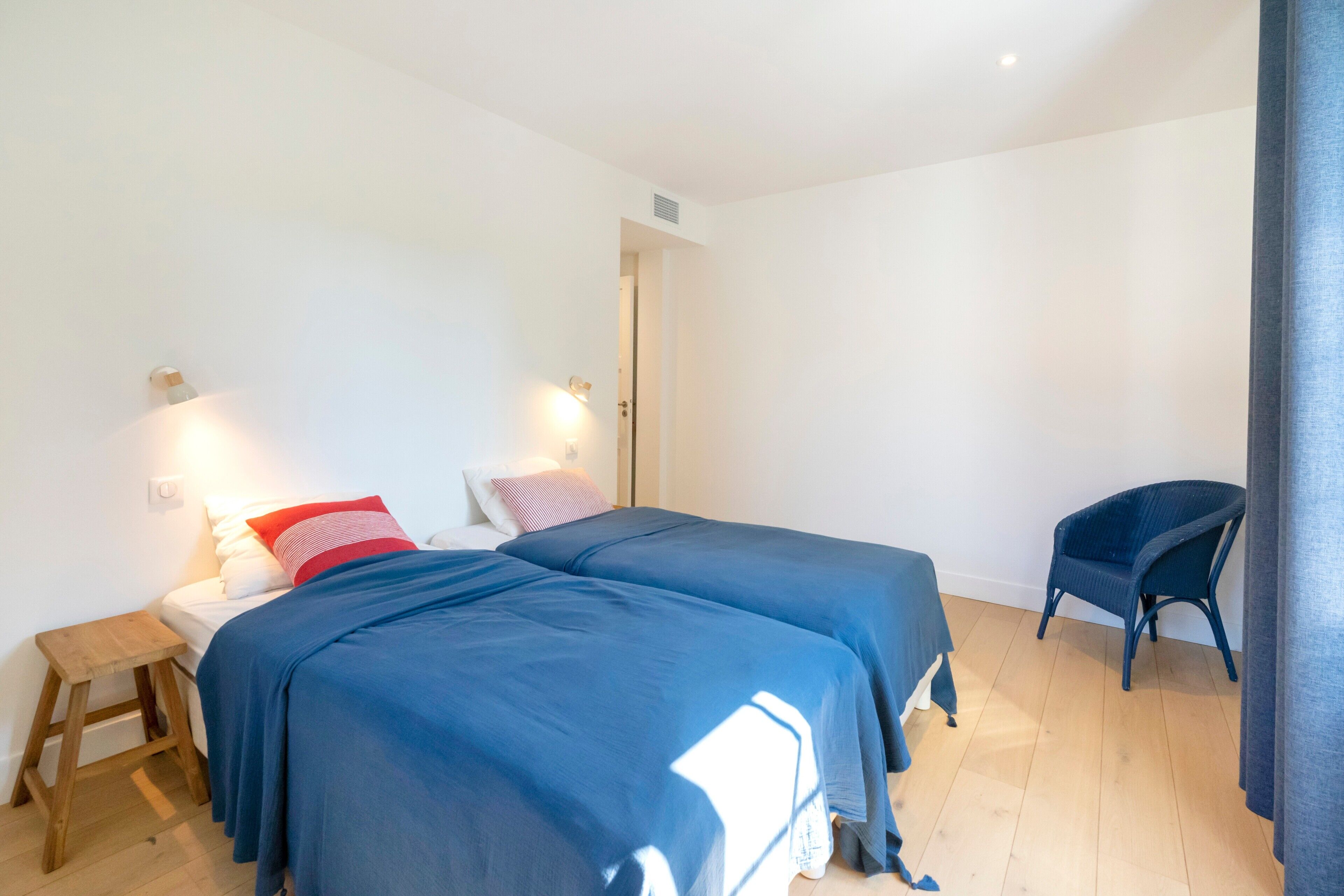 Ein Schlafzimmer mit zwei Betten, einem Holzschemel, einem Stuhl und einer Tür.