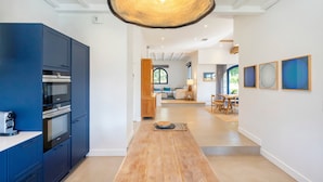 A modern kitchen with dark blue cabinets, a wooden countertop, and a hanging light fixture. - Iparra Holiday Home – Hossegor Golf – 12 Guests, Private Pool, A/C, Near the Beach (Soorts-Hossegor)