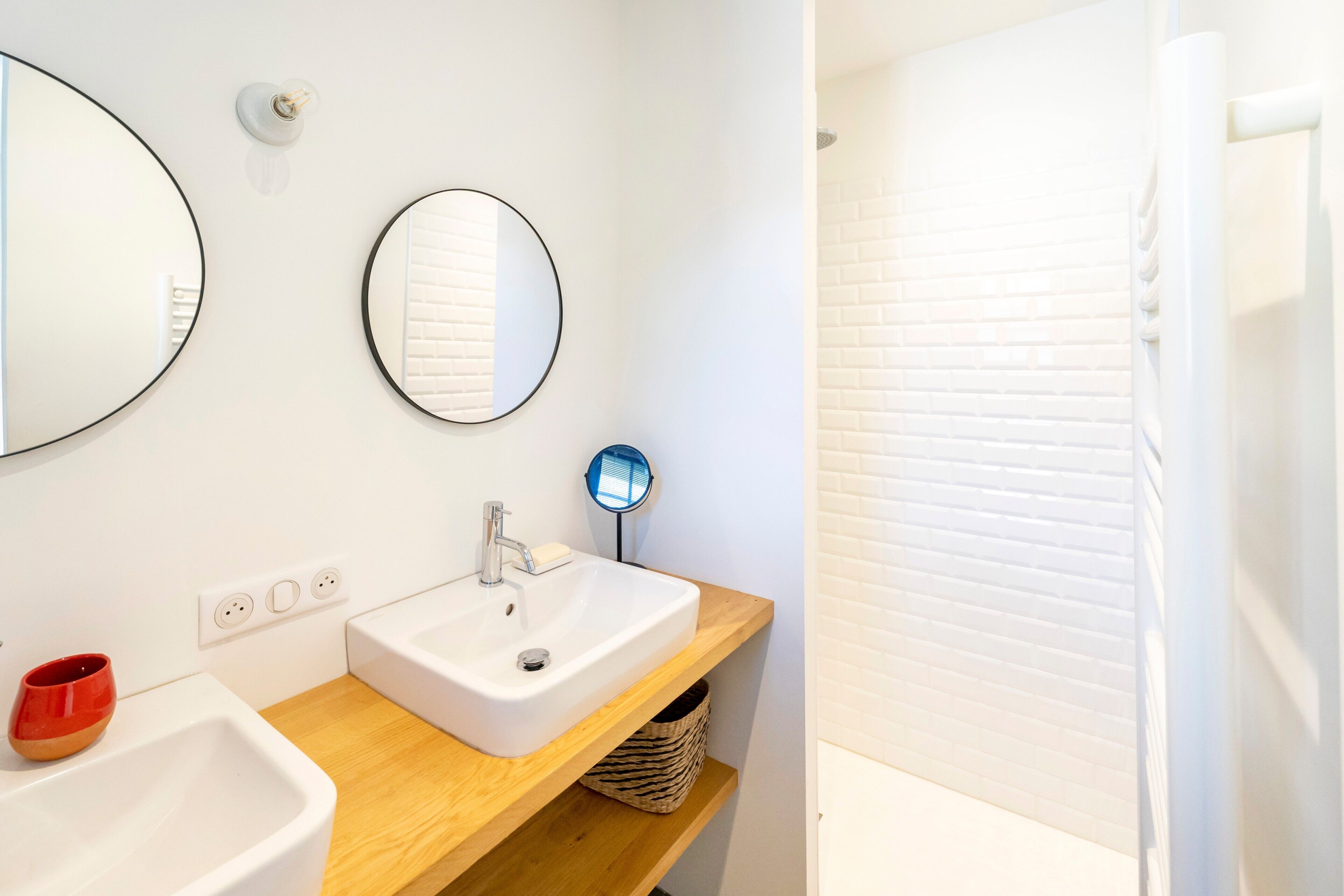 A bathroom with a white sink, a mirror, a round mirror, and a shower area.