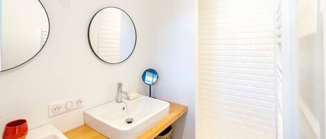 A bathroom with a white sink, a mirror, a round mirror, and a shower area.