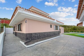 Ein modernes Haus mit Flachdach, einem Balkon und einem Swimmingpool im Hintergrund.