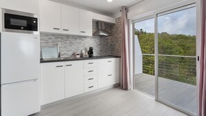 Una cocina moderna con armarios blancos, microondas integrado y un amplio ventanal corredero a un balcón con vistas a zonas verdes.