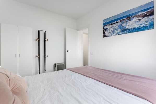 Un dormitorio con cama, radiador, una puerta y un cuadro de una escena costera.