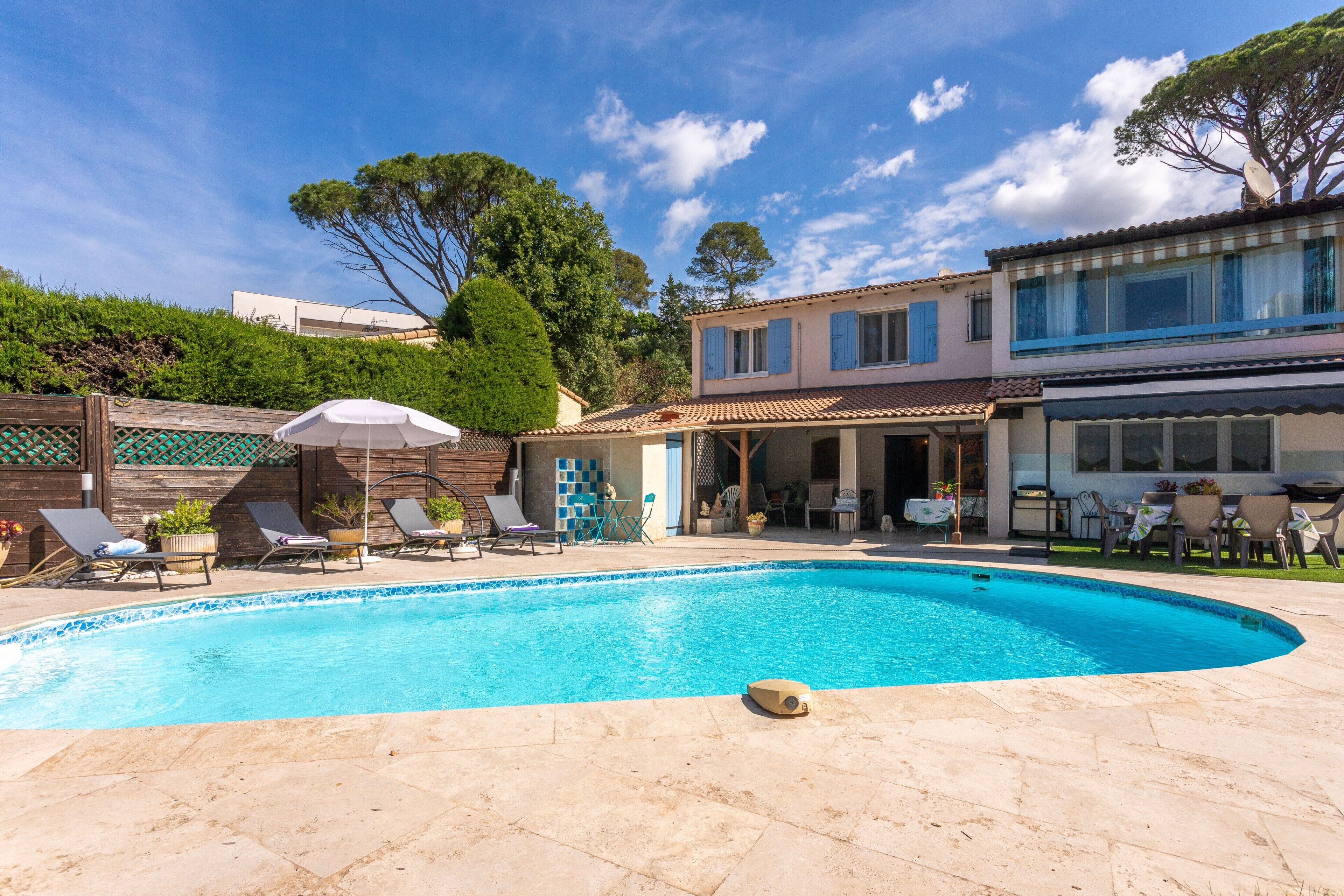 A swimming pool with lounge chairs and umbrellas, a wooden deck, and a building with a tiled roof and windows.