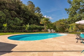 Una piscina con bordo piastrellato, circondata da vegetazione lussureggiante e alberi.