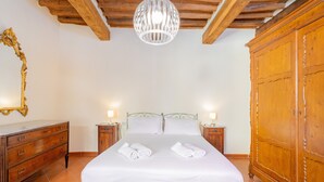Une chambre à coucher comprenant un lit, deux tables de chevet, une armoire en bois, un luminaire suspendu et un miroir au mur.