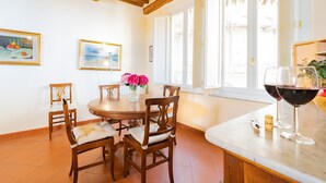 Un coin repas avec une table ronde, des chaises en bois, un vase de fleurs et un verre à vin posé sur le comptoir.