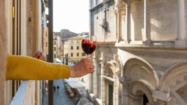 Une personne tenant un verre de vin, avec vue sur une rue bordée de bâtiments historiques.